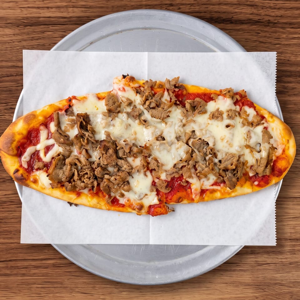Oval flatbread pizza with red sauce, melted cheese, and sliced meat on a metal pan.
