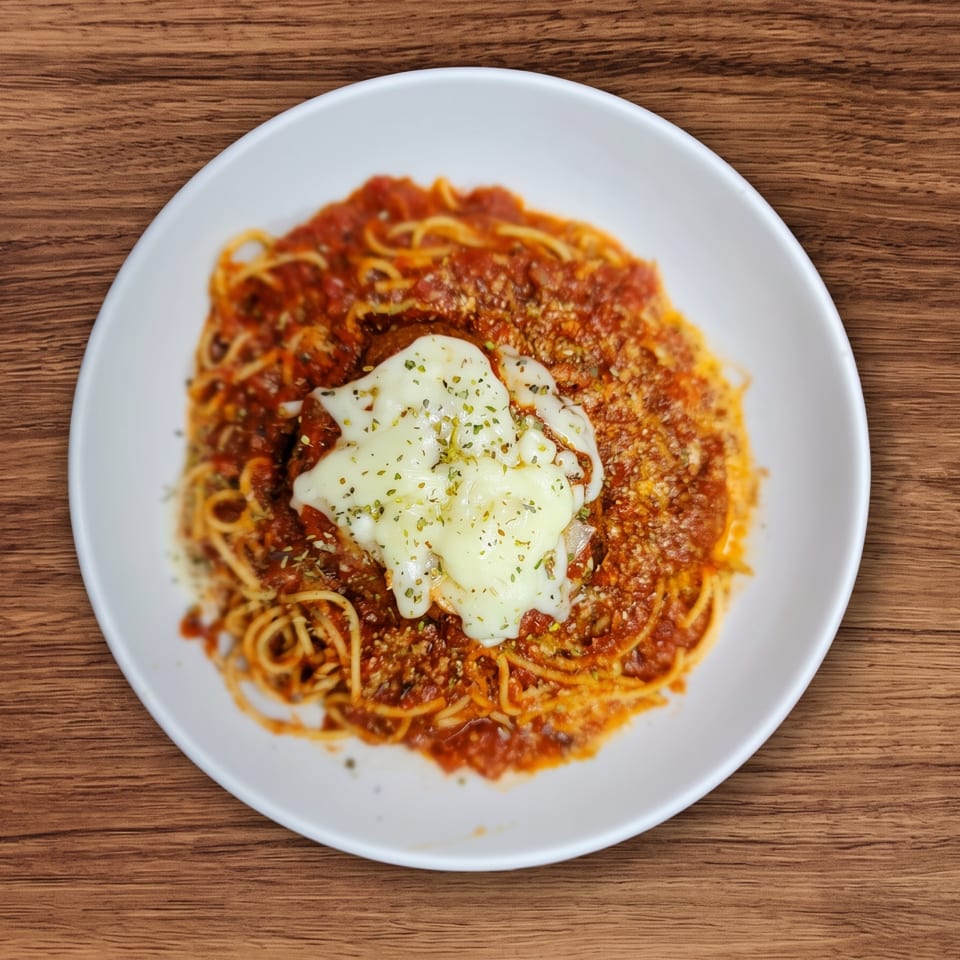 Spaghetti with red sauce, melted cheese, and herbs on a white plate over a wooden table.