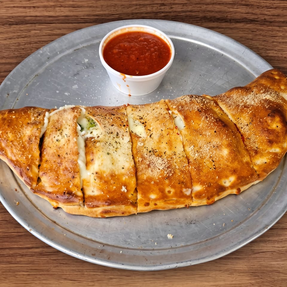 Sliced calzone with melted cheese and herbs on a metal tray, served with a side of marinara sauce.